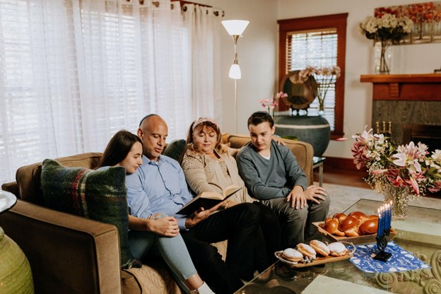 A Jewish family sits on the couch, reading a book.